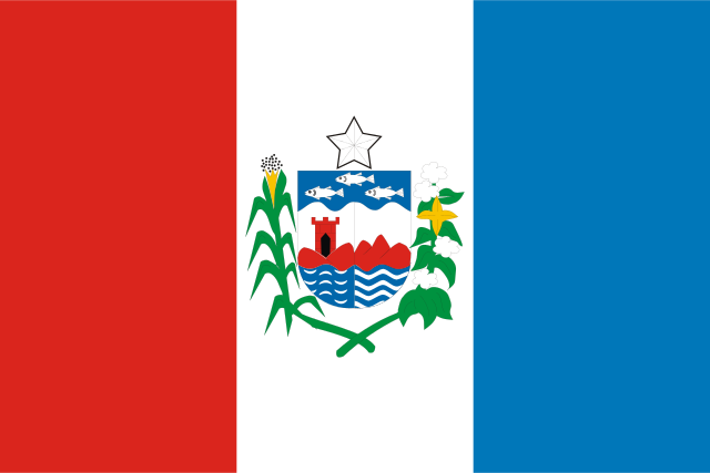 Três faixas verticais: vermelho junto ao mastro, branco e azul; no centro, um brasão com estrela, peixes e uma torre, entre ramos verdes.